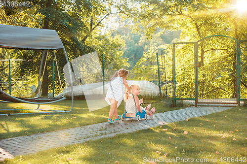 Image of Cute little blond girls riding a toy car in summer.