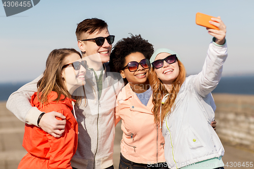 Image of happy friends taking selfie by smartphone outdoors