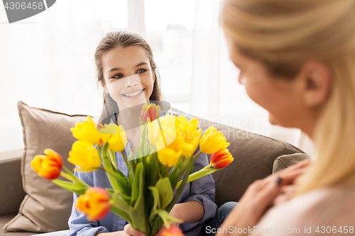 Image of happy girl giving flowers to mother at home