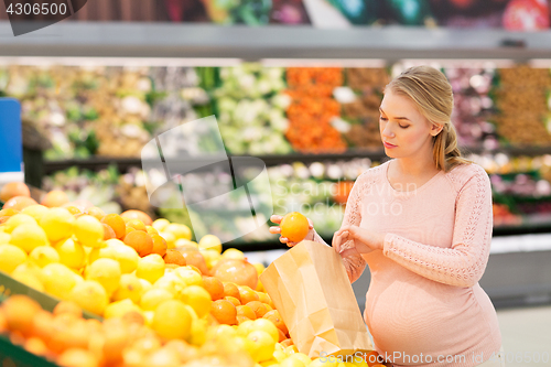 Image of pregnant woman with bag buying oranges at grocery