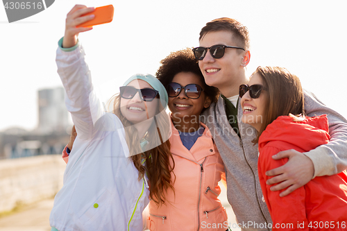 Image of happy friends taking selfie by smartphone outdoors