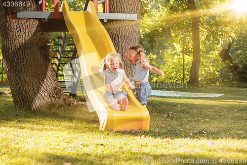 Image of Happy little girls rolling down the hill on the playground