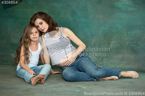 Image of Pregnant mother with teen daughter. Family studio portrait over blue background