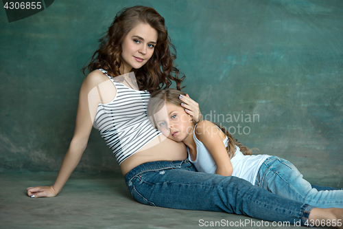 Image of Pregnant mother with teen daughter. Family studio portrait over blue background