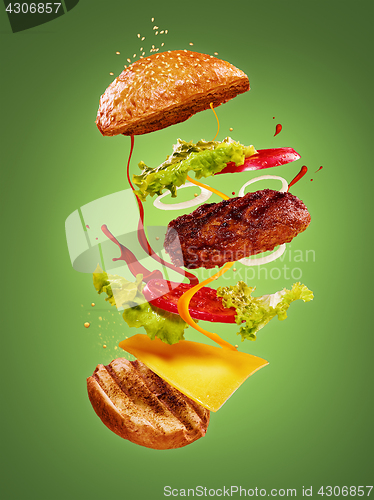 Image of The hamburger with flying ingredients on green background