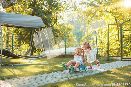 Image of Cute little blond girls riding a toy car in summer.