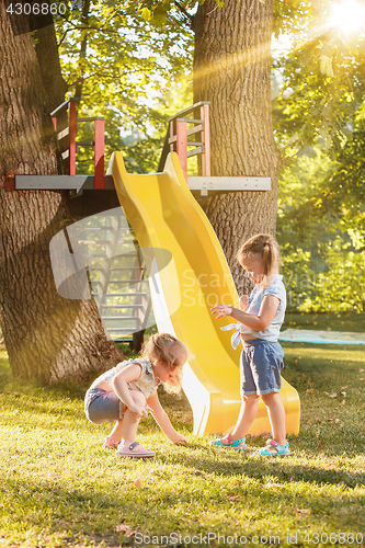 Image of Happy little girls rolling down the hill on the playground