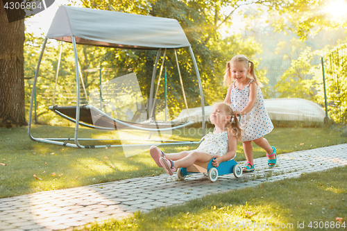 Image of Cute little blond girls riding a toy car in summer.