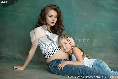 Image of Pregnant mother with teen daughter. Family studio portrait over blue background