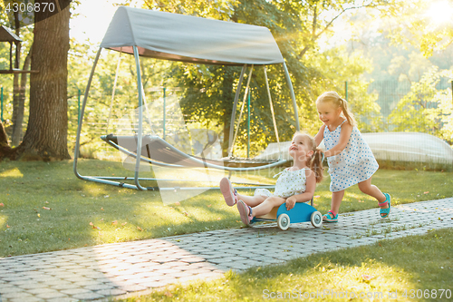 Image of Cute little blond girls riding a toy car in summer.