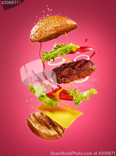 Image of The hamburger with flying ingredients on rose background