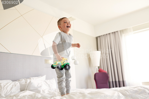 Image of happy little boy with toy car on home or hotel bed
