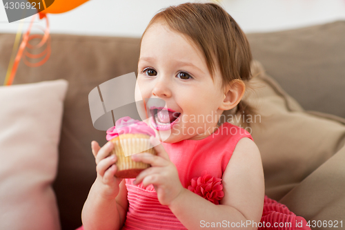 Image of happy baby girl eating cupcake on birthday party