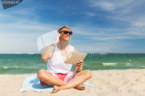 Image of happy man with tablet pc and headphones on beach