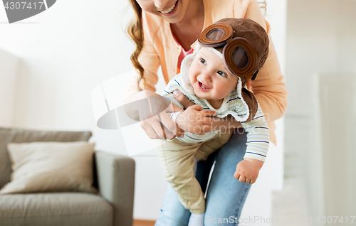 Image of happy mother with baby wearing pilot hat at home