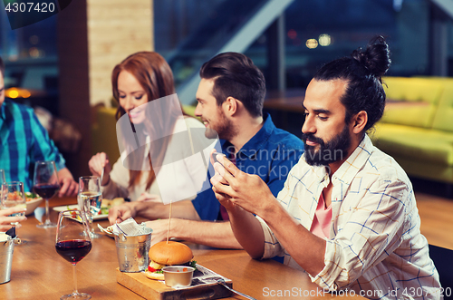 Image of man with smartphone and friends at restaurant