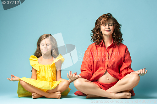 Image of Pregnant mother with teen daughter. Family studio portrait over blue background