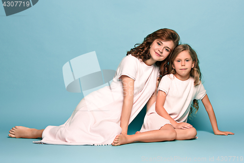 Image of Pregnant mother with teen daughter. Family studio portrait over blue background