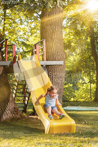 Image of Happy little girl rolling down the hill on the playground