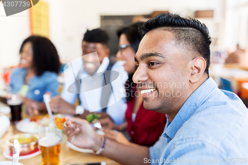 Image of happy friends eating and talking at restaurant