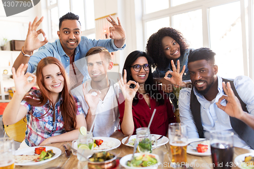 Image of happy friends showing ok hand sign at restaurant
