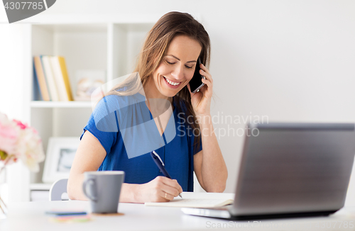 Image of woman with notepad calling on smartphone at office