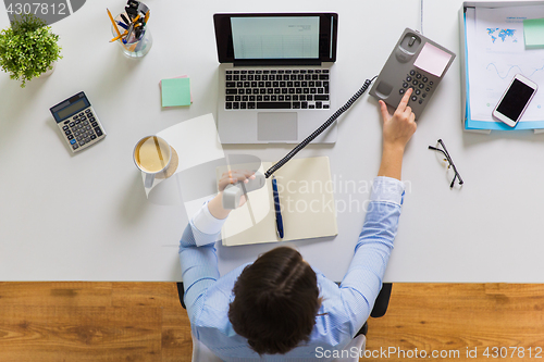 Image of businesswoman calling on phone at office table