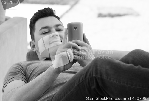 Image of Young man using mobile while lying on couch