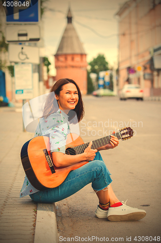 Image of fun smiling woman with a guitar sits on the curb