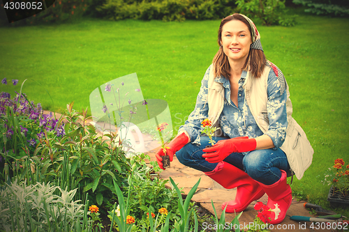 Image of smiling woman in kerchief and red boots planting flowers