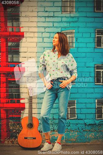 Image of smiling woman in jeans and a blue shirt stands against the wall 