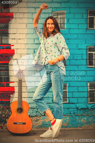 Image of smiling woman in jeans stands near wall with graffiti next to gu