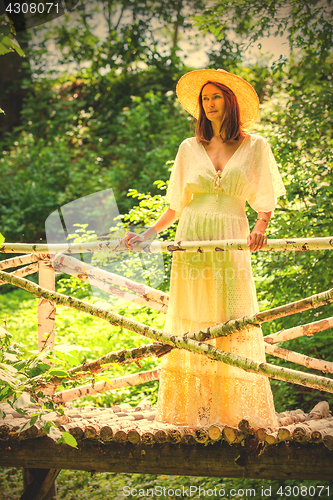 Image of Beautiful woman in a white summer dress and a straw hat stands o