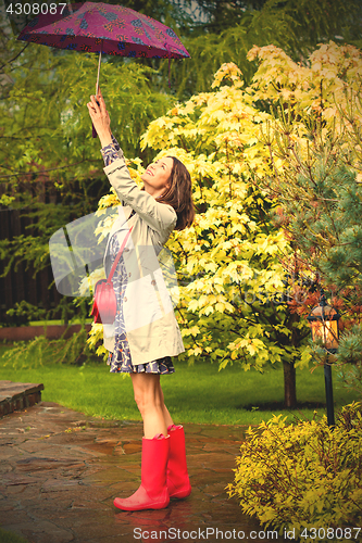 Image of Beautiful smiling woman in red rubber boots and with an umbrella
