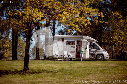 Image of Woman is standing with a mug of coffee near the camper.