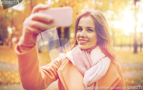 Image of woman taking selfie by smartphone in autumn park