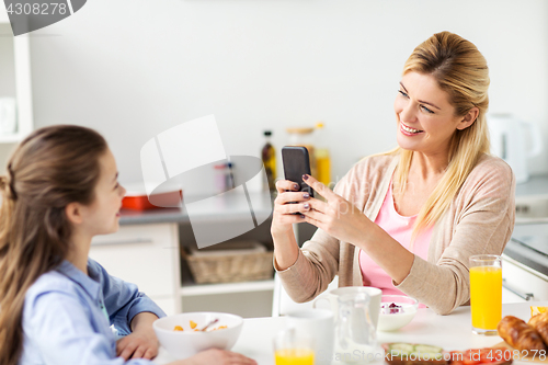 Image of woman photographing daughter by smartphone at home