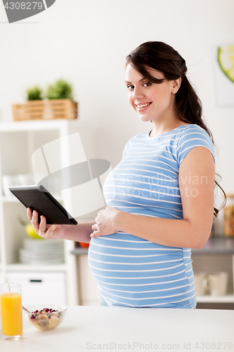 Image of pregnant woman with tablet pc eating at home