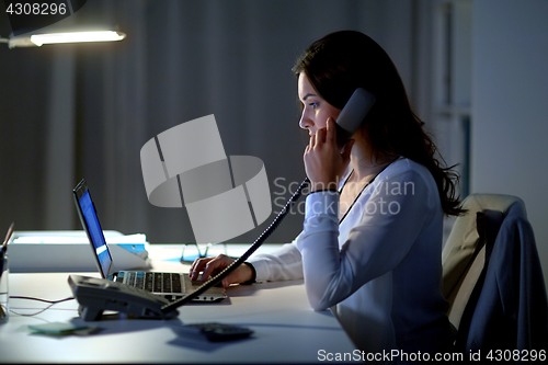 Image of woman with laptop calling on phone at night office