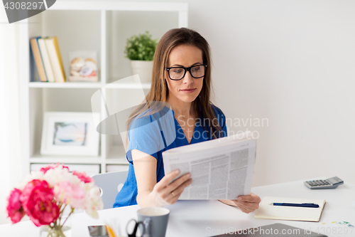 Image of woman in glasses reading newspaper at office