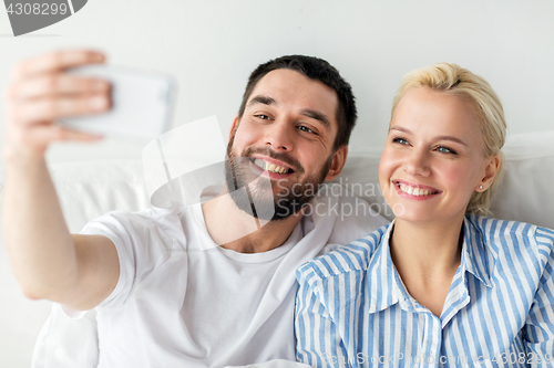 Image of happy couple with smartphone taking selfie at home