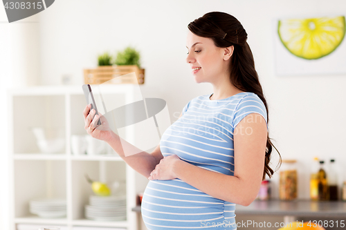 Image of happy pregnant woman with smartphone at kitchen