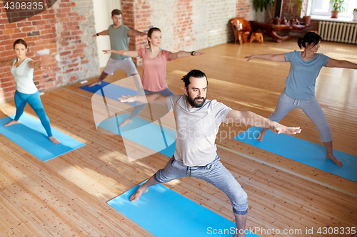 Image of group of people doing yoga warrior pose at studio