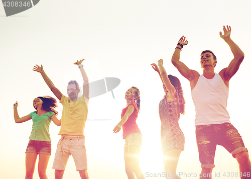 Image of smiling friends dancing on summer beach