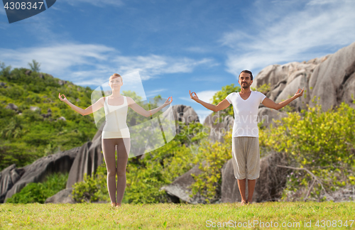 Image of happy couple making yoga exercises on beach