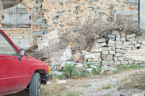 Image of Old rusty red car parked near the wall