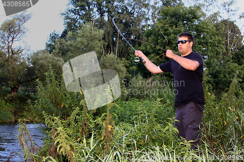 Image of Young man with fishing rod fishing at a river