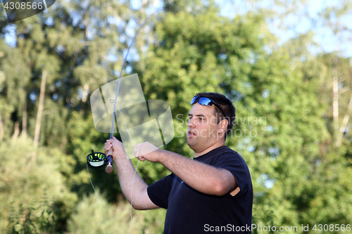 Image of Young man with fishing rod fishing at a river