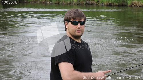 Image of Young man with fishing rod fishing at a river