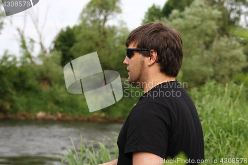 Image of Young man with fishing rod fishing at a river